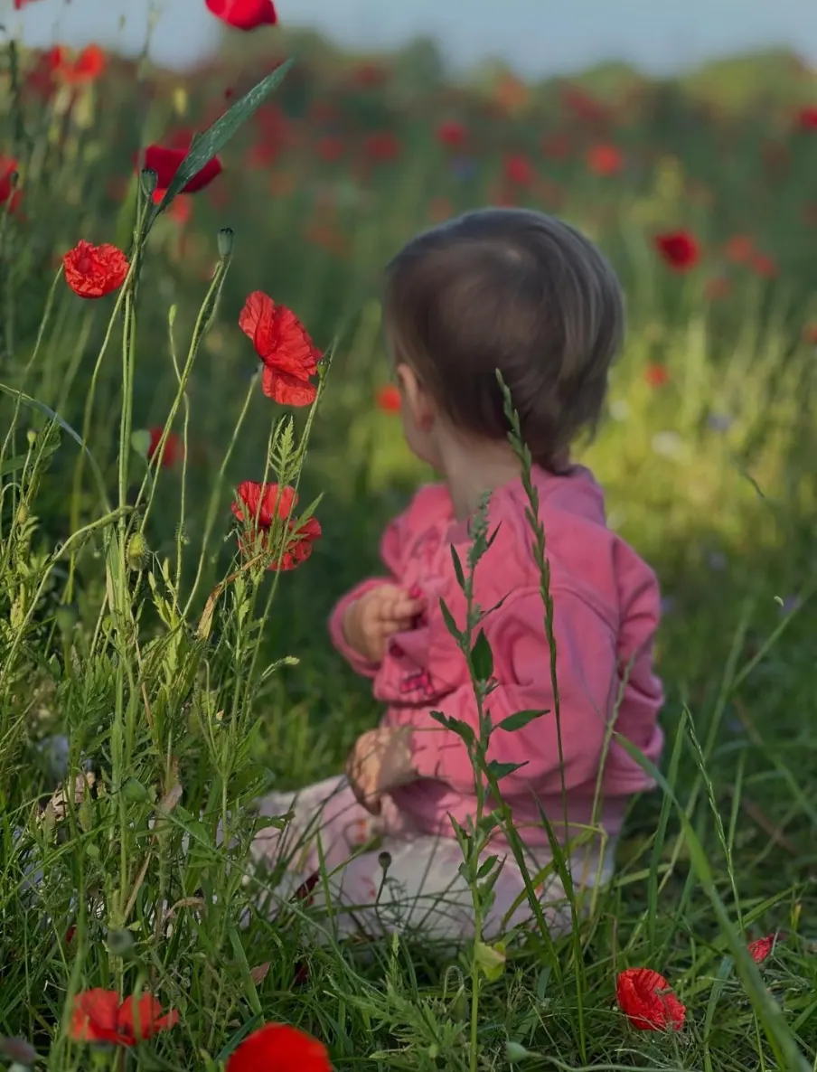 Jong kind in roze zit buiten tussen klaprozen in het gras