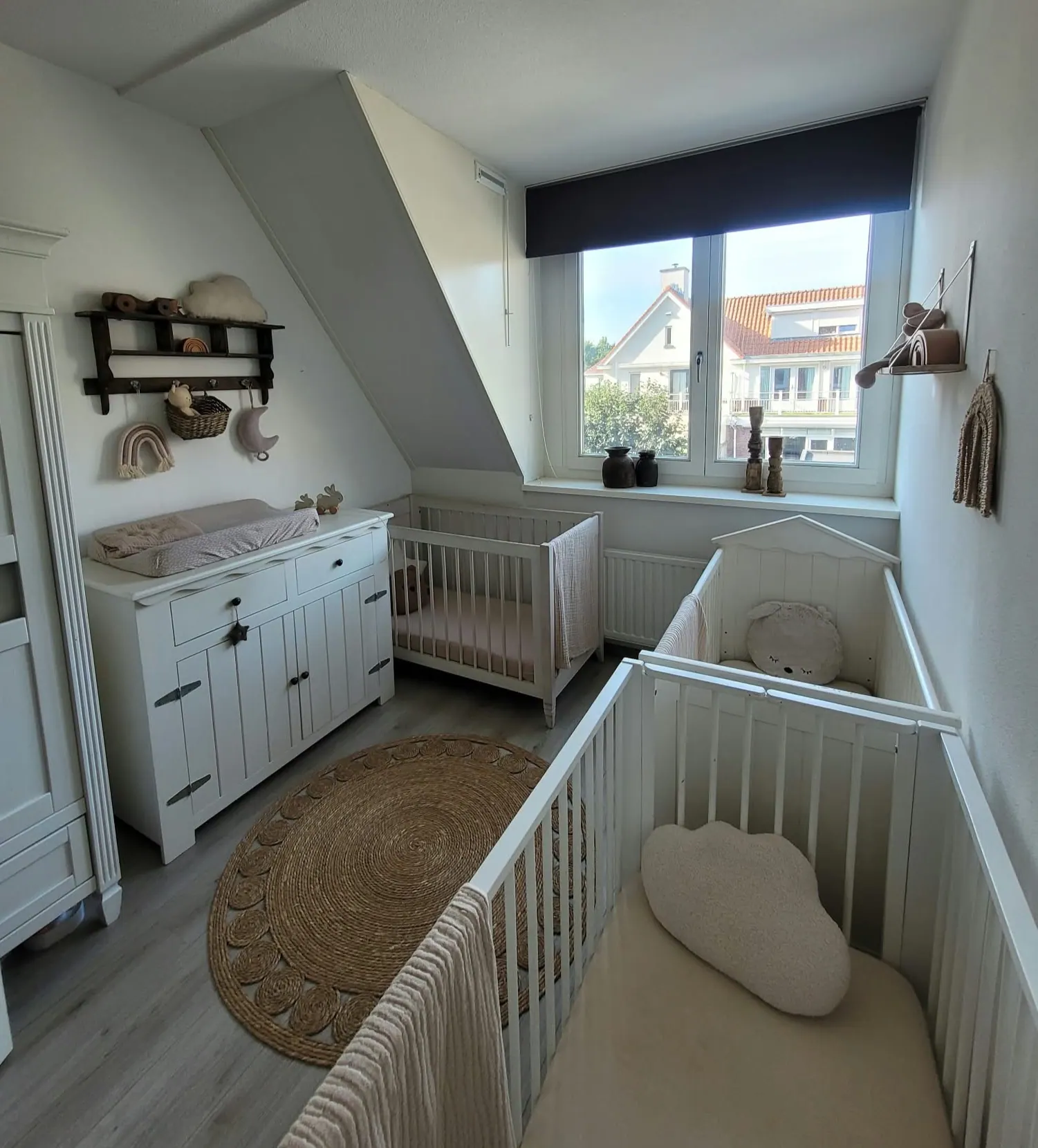 Lichte babykamer met twee ledikanten, commode en rond vloerkleed