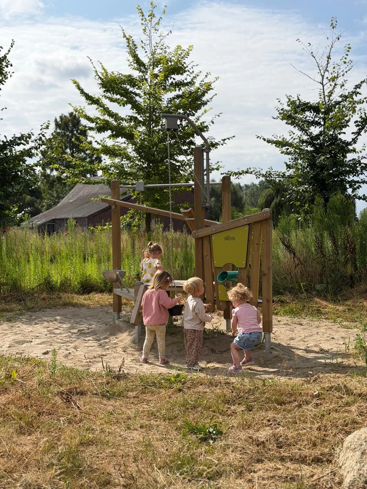 Kinderen spelen buiten in de zandbak bij een houten speeltoestel